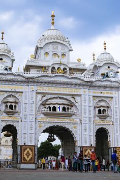 This may contain: people are standing in front of an ornate white building with gold trimmings and arches