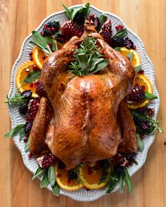 This may contain: a roasted turkey on a platter with oranges and berries