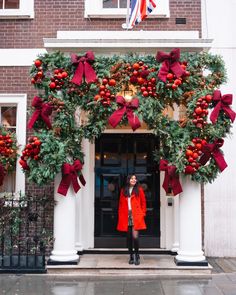 This may contain: a woman standing in front of a building decorated with christmas wreaths and pomegranates