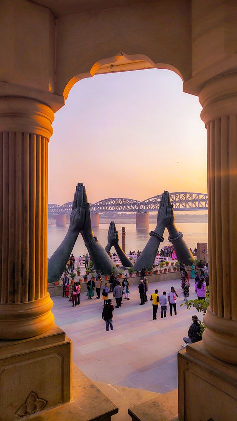 This may contain: people are standing around in front of some pillars and looking out at the water with a bridge in the background