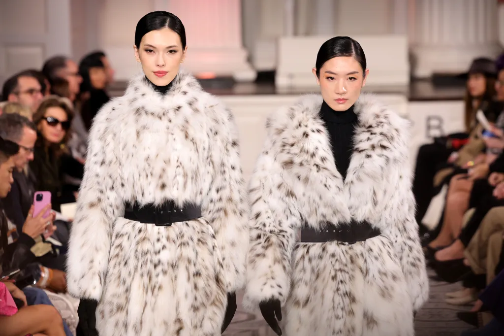 Two models in spotted fur coats walking a runway.