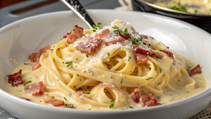 This may contain: pasta with bacon and parmesan cheese in a white bowl