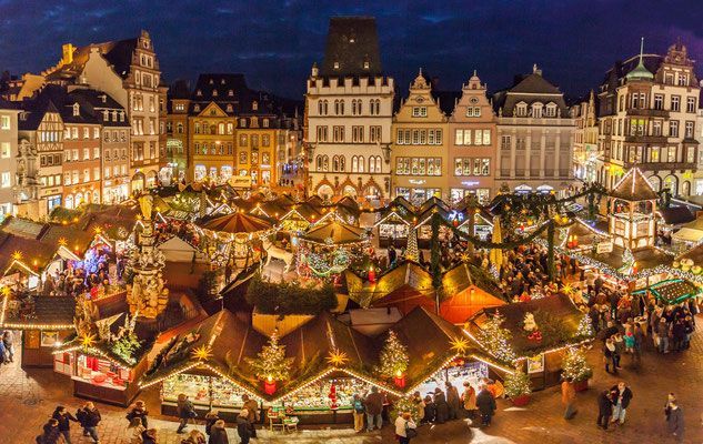 This may contain: an aerial view of a christmas market in europe at night with people walking around it
