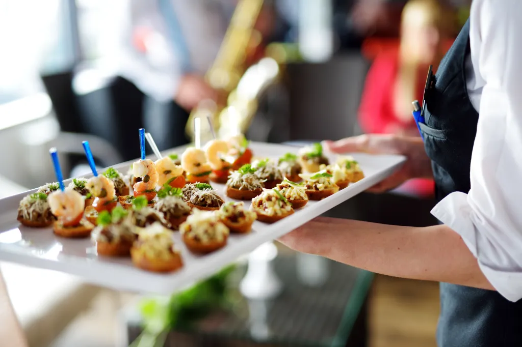 Waiter carrying a tray of appetizers including shrimp and other meat dishes.