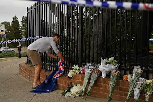 People offered flowers at Bondi Beach. A man tying an Australian flag near the monument. (Source- The Age)