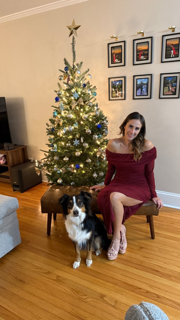 Fernanda Aceves in a red dress with a dog next to a Christmas tree.