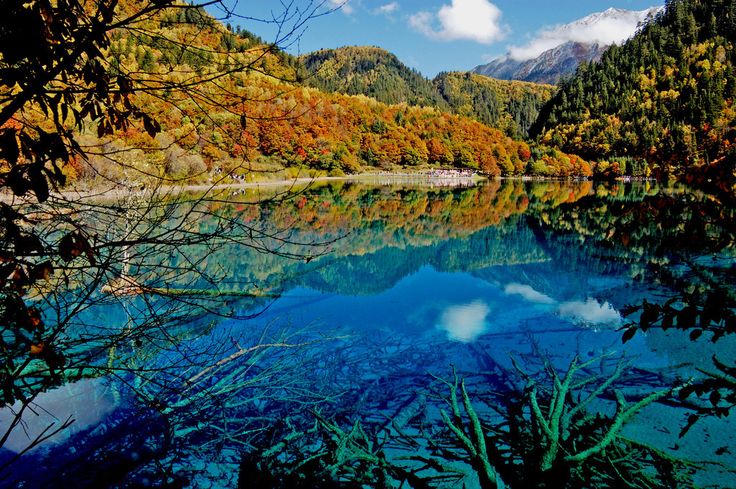 This may contain: a lake surrounded by trees with mountains in the background and blue sky reflected in the water