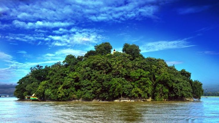 This may contain: an island in the middle of water with trees on top and blue sky above it