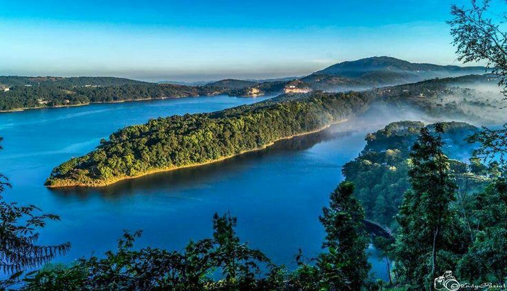 This may contain: an island in the middle of a lake surrounded by trees and foggy water on a sunny day