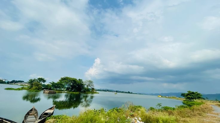This may contain: two canoes sitting on the shore of a lake with trees in the background and clouds in the sky