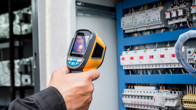Hand pointing a thermal camera at electrical equipment