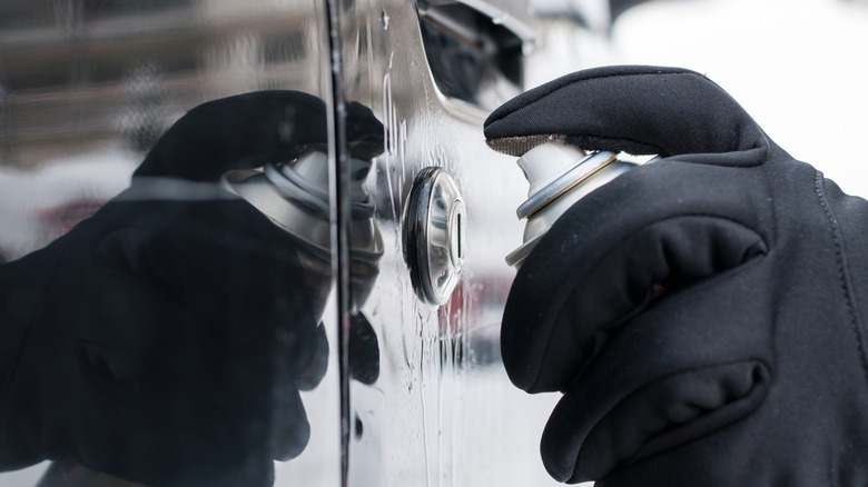 Gloved hand using spray product to de-ice vehicle door lock