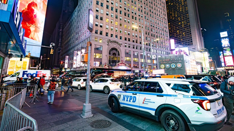Times square at night with nypd police vehicle, heavy traffic, bright billboards, and crowds in New York City.