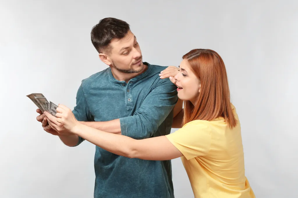 A woman in a yellow shirt reaching for money held by a man in a blue shirt.