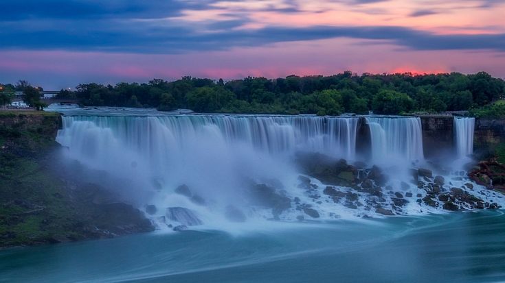 This may contain: a waterfall with water pouring from it at sunset