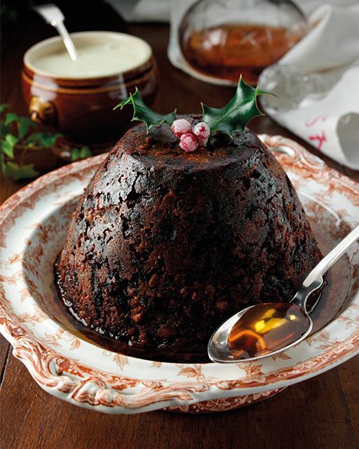 This may contain: a chocolate cake with holly on top in a bowl and spoon next to the plate