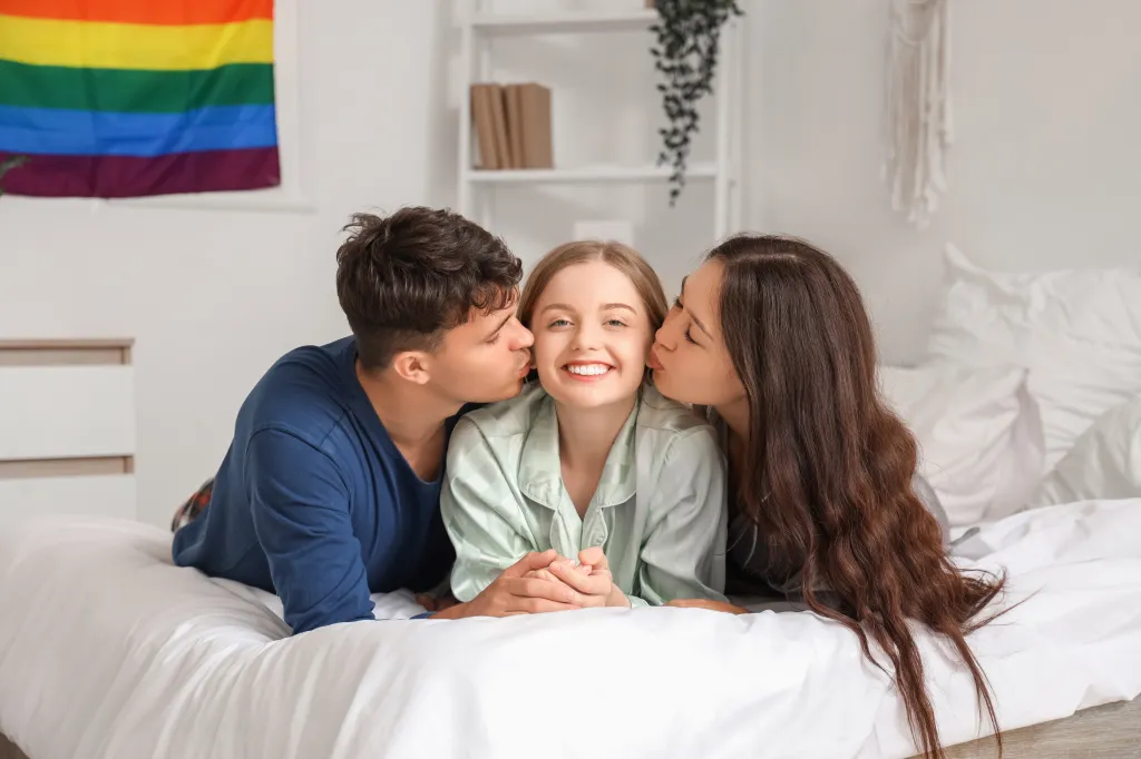 Young man and two women kissing in the bedroom.