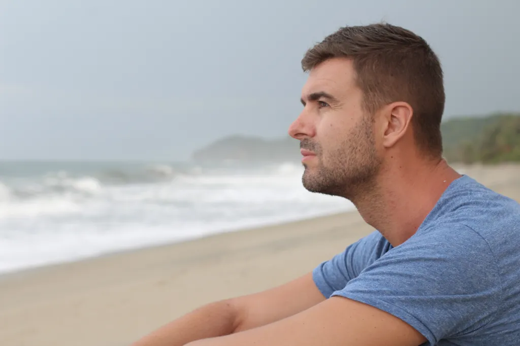 Man on the beach looking thoughtfully into the distance.