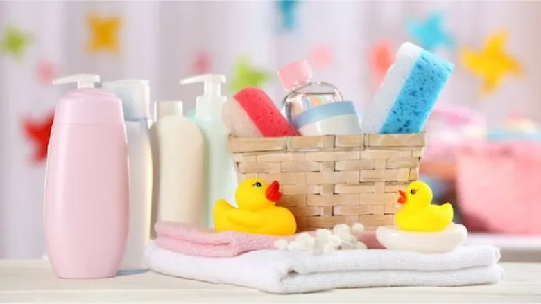 Baby bath essentials arranged on a table, including baby lotion and shampoo bottles, soft towels, colorful sponges, cotton balls, and yellow rubber ducks.