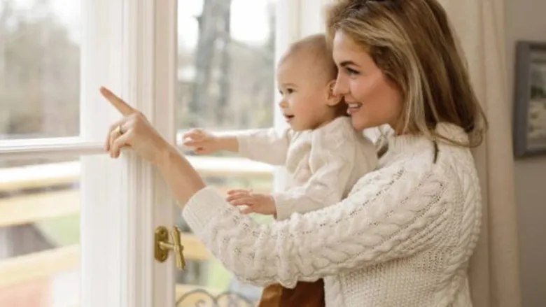 baby wearing swear is with her mom, looking outside window