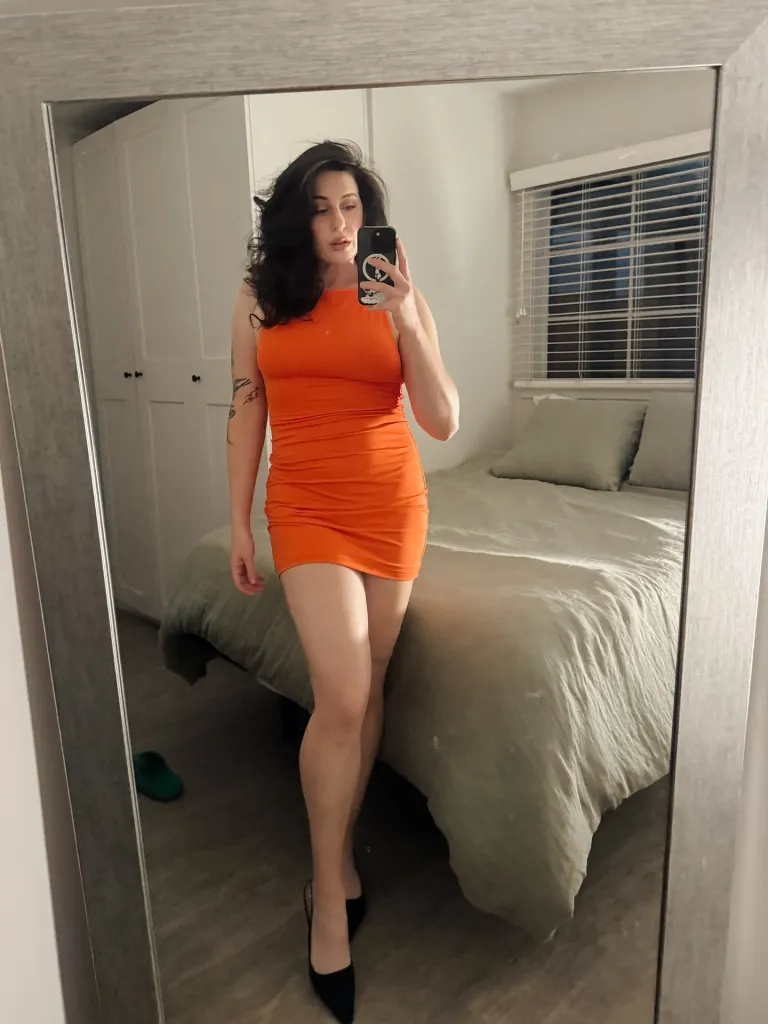 A woman in an orange dress taking a mirror selfie.