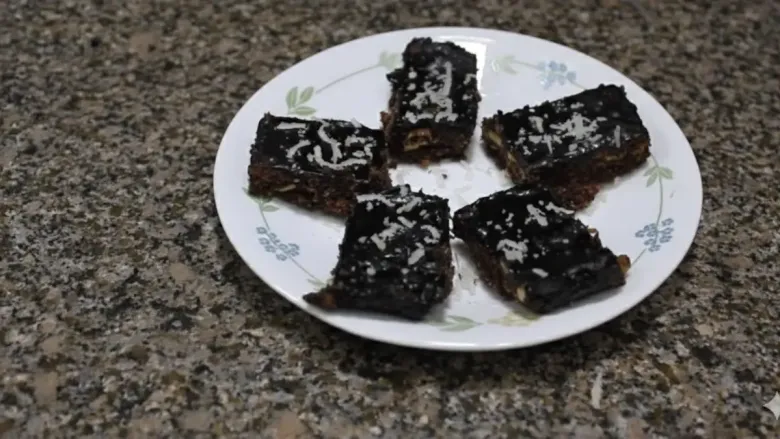 Chocolate fudge pieces topped with coconut, served on a white plate.