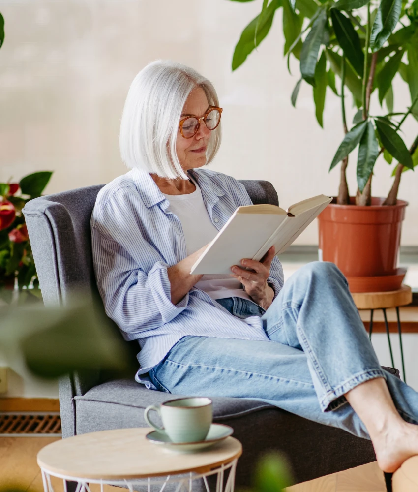 older woman sitting in chair reading book happy being alone