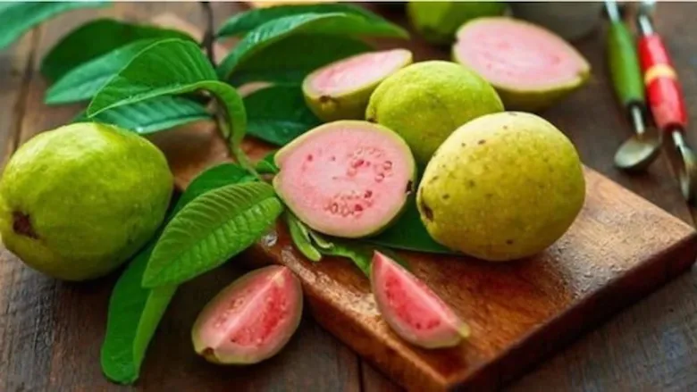 Fresh guava fruit, whole and sliced, showing its green skin and pinkish-white interior with seeds.
