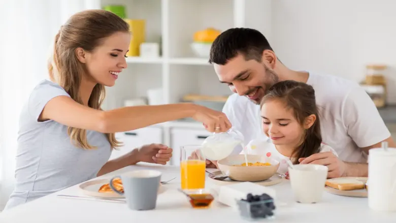 woman pouring milk in the bowl infront of man ans girl