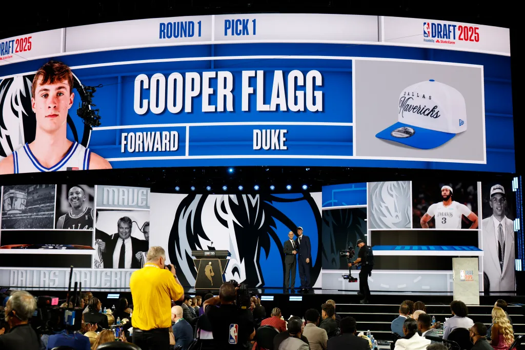 The NBA Draft 2025 stage shows Cooper Flagg as the first pick, a forward from Duke, joining the Dallas Mavericks, with two men standing on stage.
