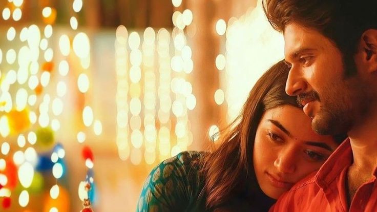 This may contain: a man and woman are looking at a cell phone in front of some christmas lights