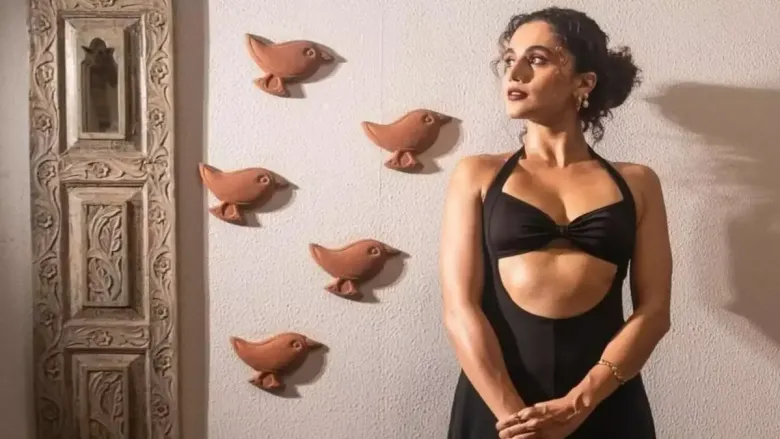 Woman in black outfit posing beside wall decor.
