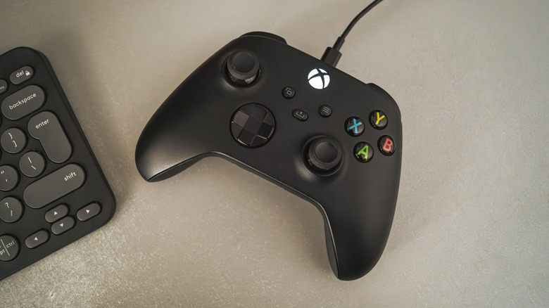 A black Xbox Controller with the cable plugged in on a light gray desk, Logitech MX Pebble keyboard slightly off-screen