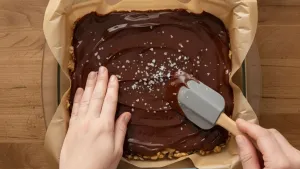 Spreading melted chocolate over nut bars and sprinkling sea salt.