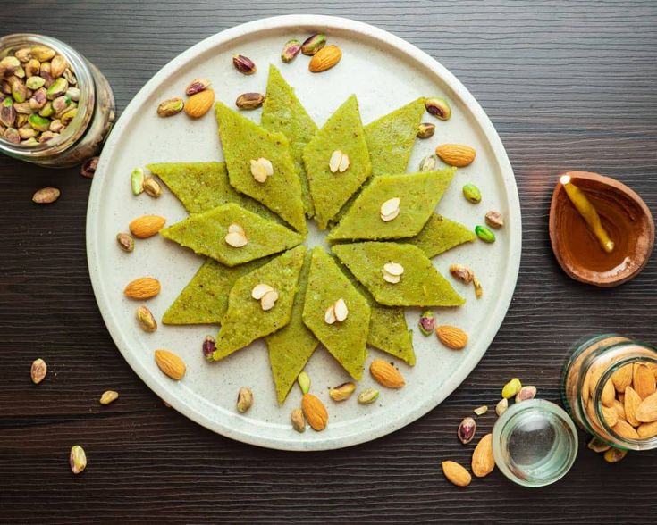 This may contain: a white plate topped with green pancakes covered in almonds and pistachio seeds