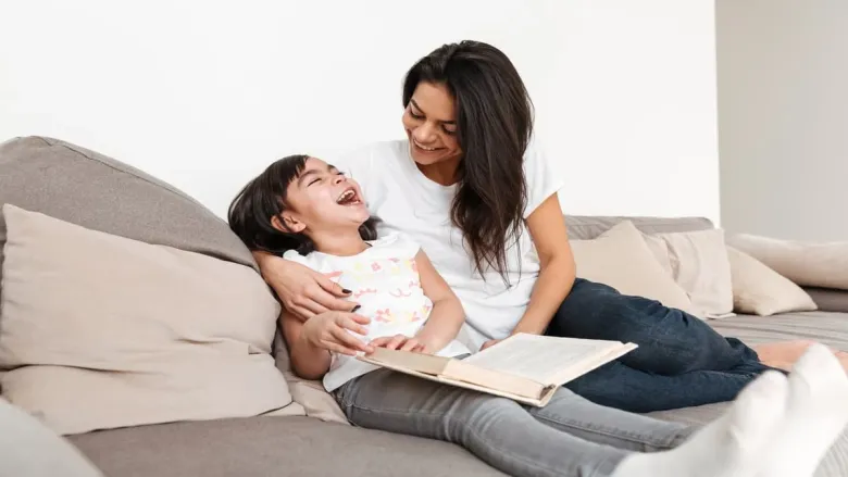 a girl holding a book and laughing with her mom