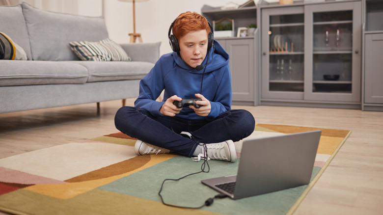 Child sitting on the floor, playing video games on a laptop.