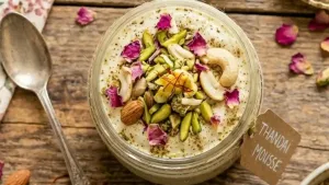 Pour the prepared mousse into serving glasses or bowls and garnish with almonds, pistachios, and rose petals.