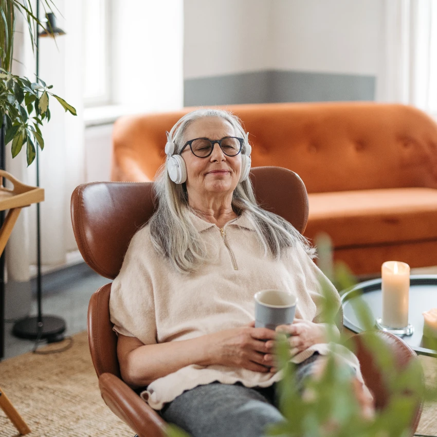 older woman listening to music while relaxing in chair with mug