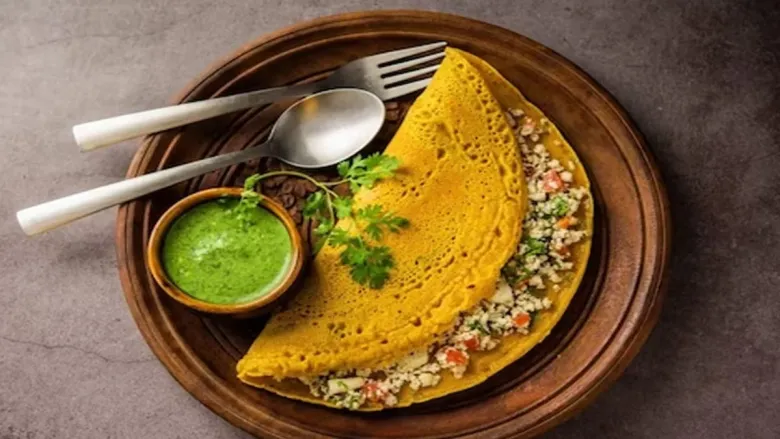 Freshly cooked poha chilla on a pan, topped with veggies and served for a nutritious morning meal.