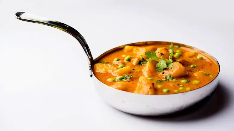 Bowl of creamy potato dish with peas, garnished with fresh coriander leaves.
