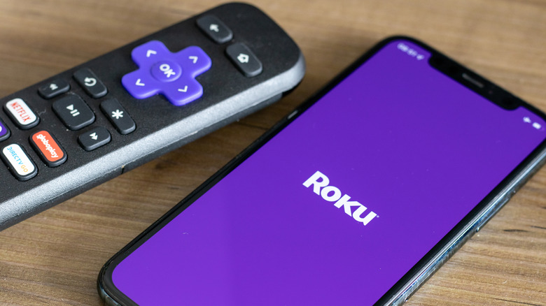 A Roku remote beside a phone with the Roku app open
