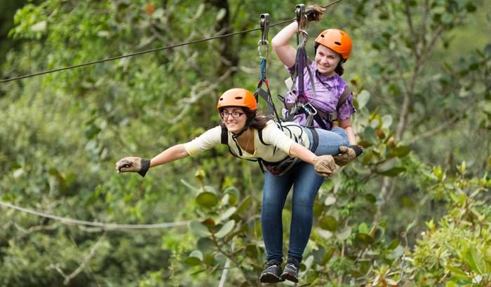 This may contain: two women are zipping through the air on a rope course in an outdoor area