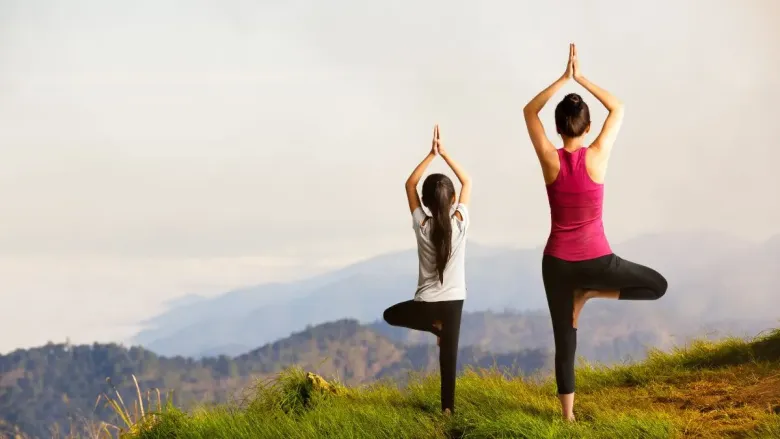 Mother and daughter performing Vrikshasana (Tree Pose) yoga together with hands in prayer position.