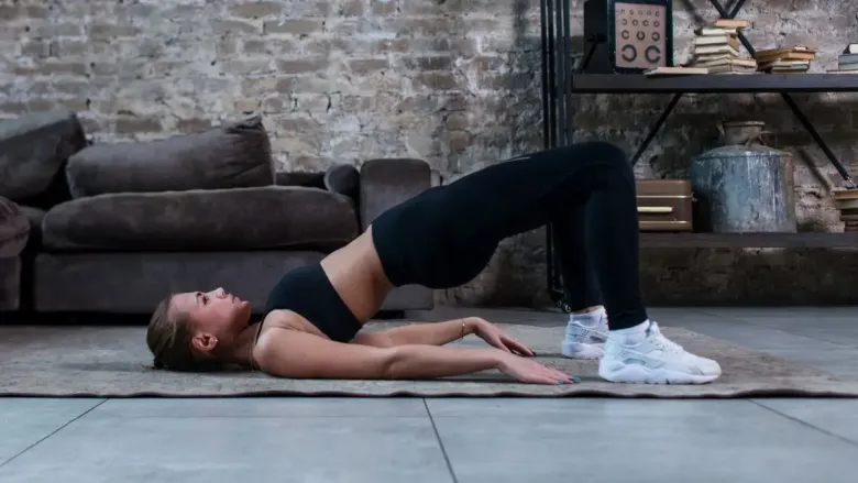 Woman performing Setu Bandhasana (Bridge Pose) yoga with hips lifted and feet on the floor.