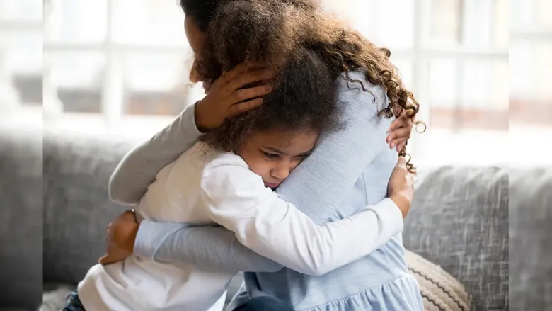 Child hugging a woman tightly on a couch, looking sad while being comforted.