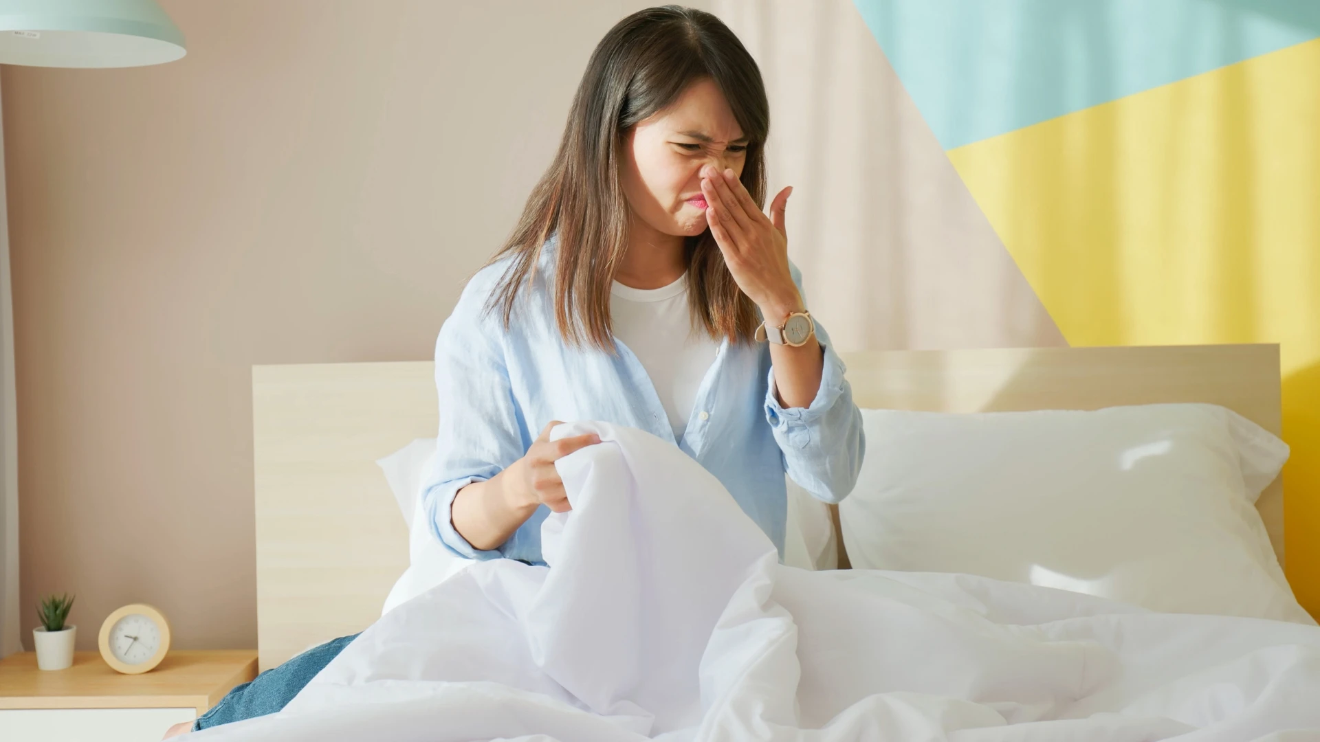 woman smelling odor after waiting too long to wash her bed sheets