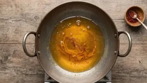 Preparing sugar syrup in a large pan and adding crushed saffron along with a little food color for fragrance and color.
