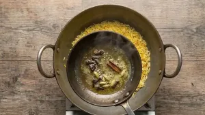 Heating ghee in a small pan and adding cloves, cardamom, and cinnamon to prepare a fragrant tempering.