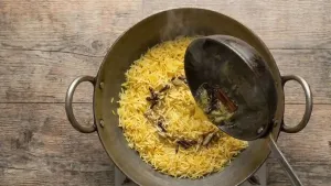 Pouring the aromatic ghee tempering over the sweet rice and gently mixing so the grains remain separate.